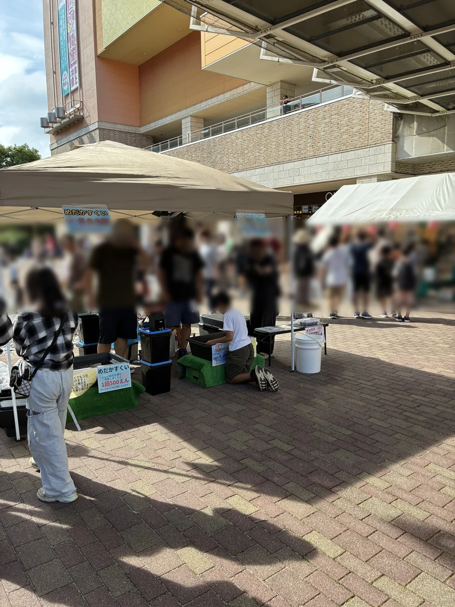 お祭りのめだかすくいの出店とにぎわう人たち